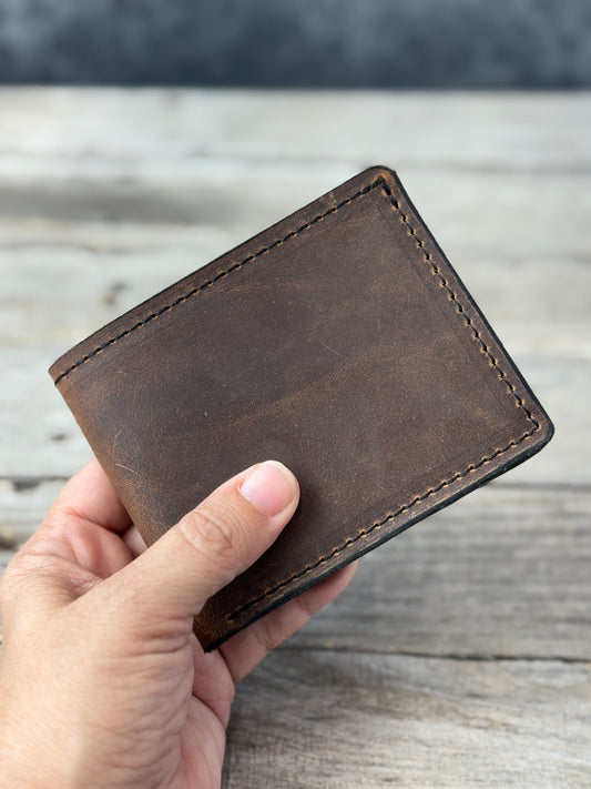 Dark brown oil tanned leather bifold wallet held in hand