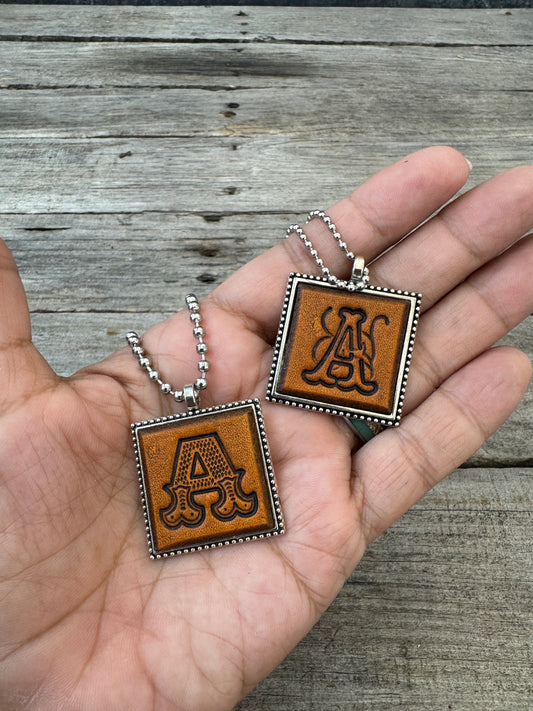 Western Block and Floral Script letter A leather pendants held in hand to show their 1-inch size