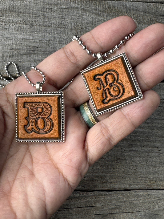 Western Block and Floral Script letter B leather pendants held in hand to show their 1-inch size