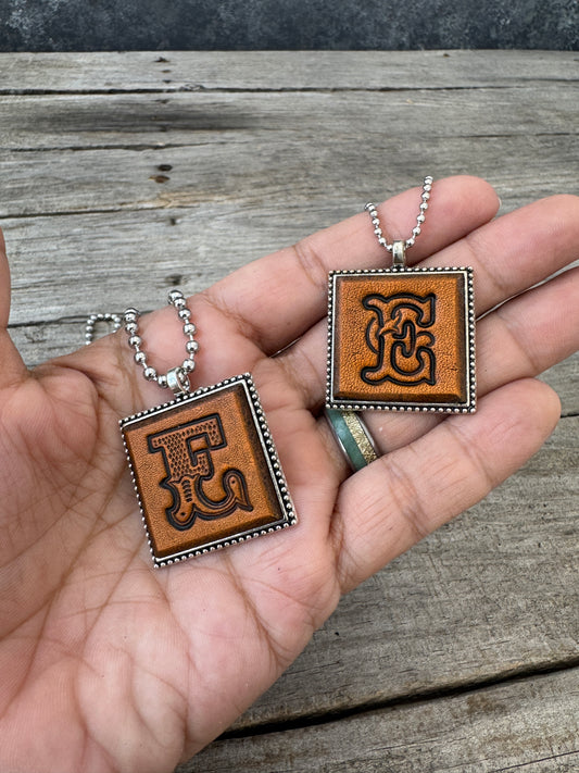 Western Block and Floral Script letter E leather pendants held in hand to show their 1-inch size