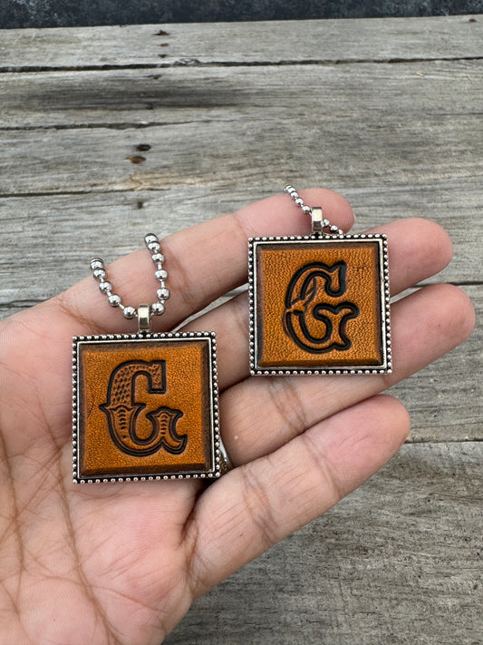 Western Block and Floral Script letter G leather pendants held in hand to show their 1-inch size