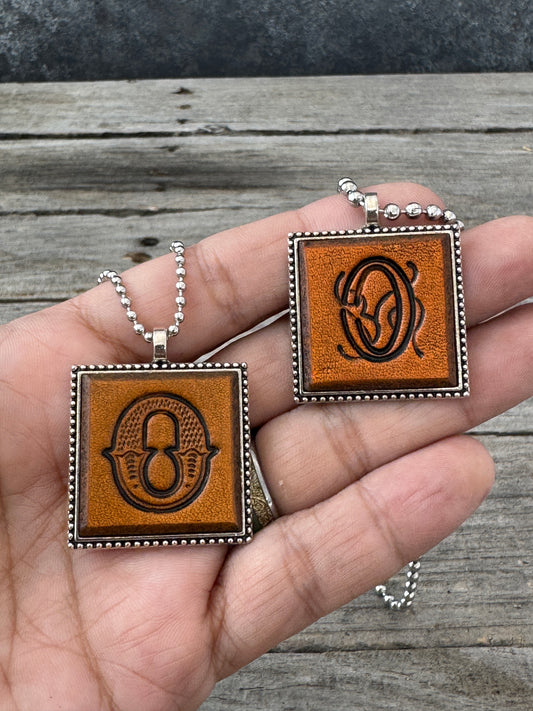 Western Block and Floral Script Letter O leather necklaces held in hand for size comparison