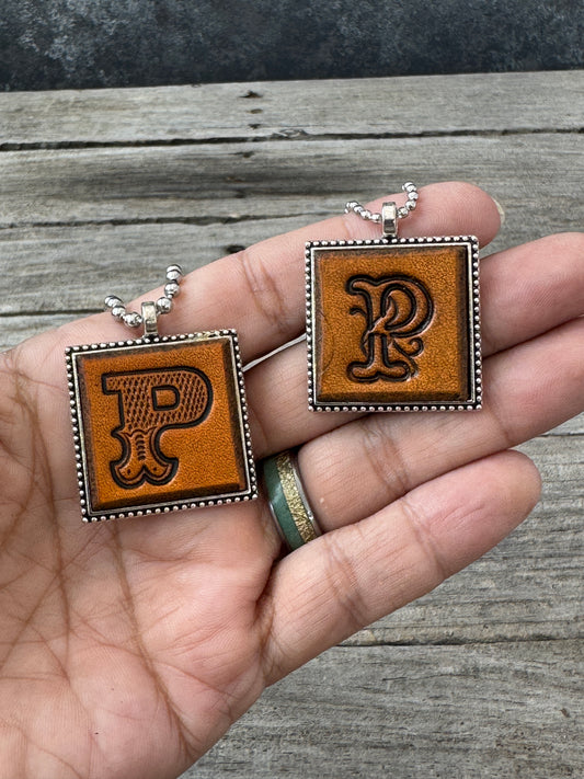 Western Block and Floral Script Letter P leather necklaces held in hand for size comparison