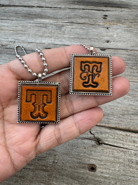Western Block and Floral Script Letter T leather necklaces held in hand for size comparison