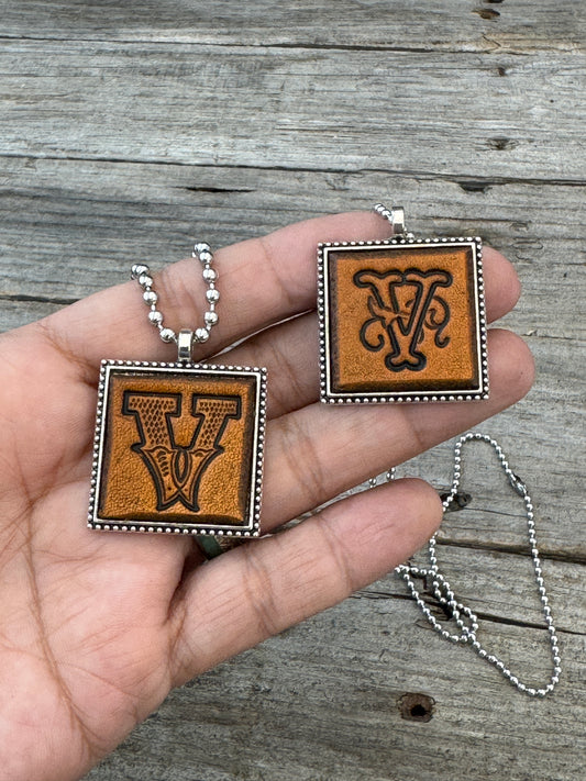 Western Block and Floral Script Letter V leather necklaces held in hand for size comparison
