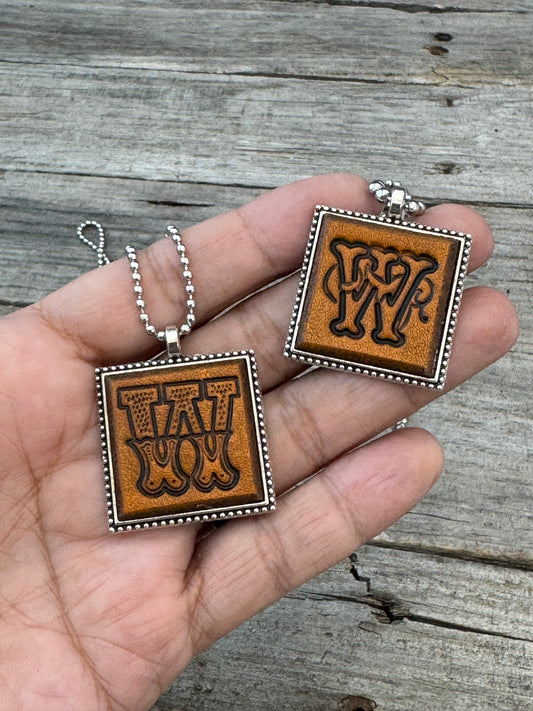 Western Block and Floral Script Letter W leather necklaces held in hand for size comparison
