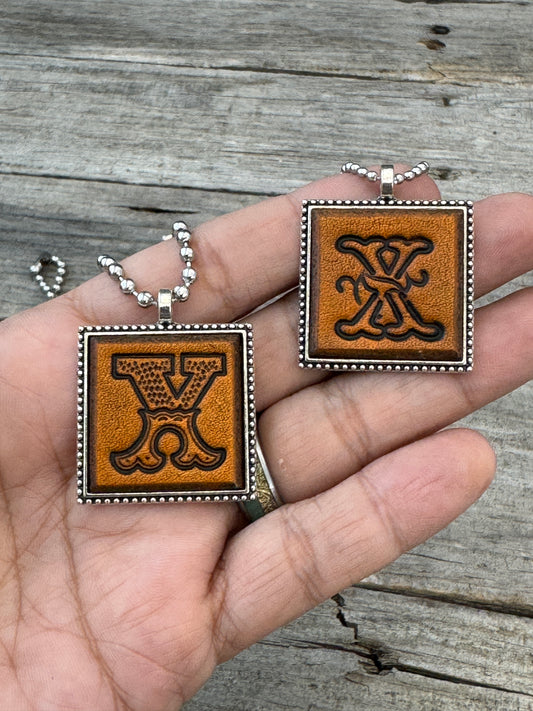 Western Block and Floral Script Letter X leather necklaces held in hand for size comparison