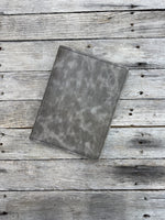 Grey oil tanned leather composition notebook cover with natural pull-up variation and black stitching.