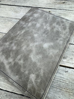 Grey oil tanned leather composition notebook cover with natural pull-up variation and black stitching.