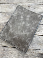 Grey oil tanned leather composition notebook cover with natural pull-up variation and black stitching.
