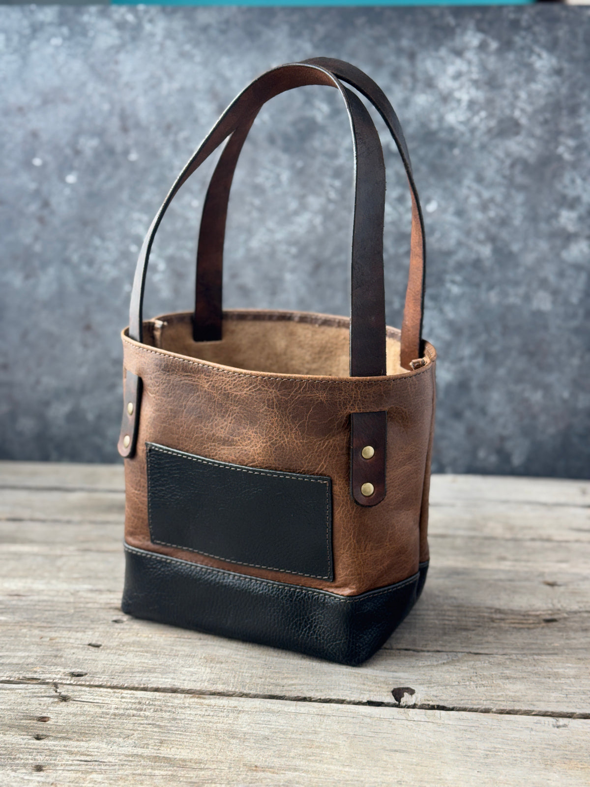 Mini two-tone bison leather tote in vintage sand and black with exterior pocket and brown leather straps