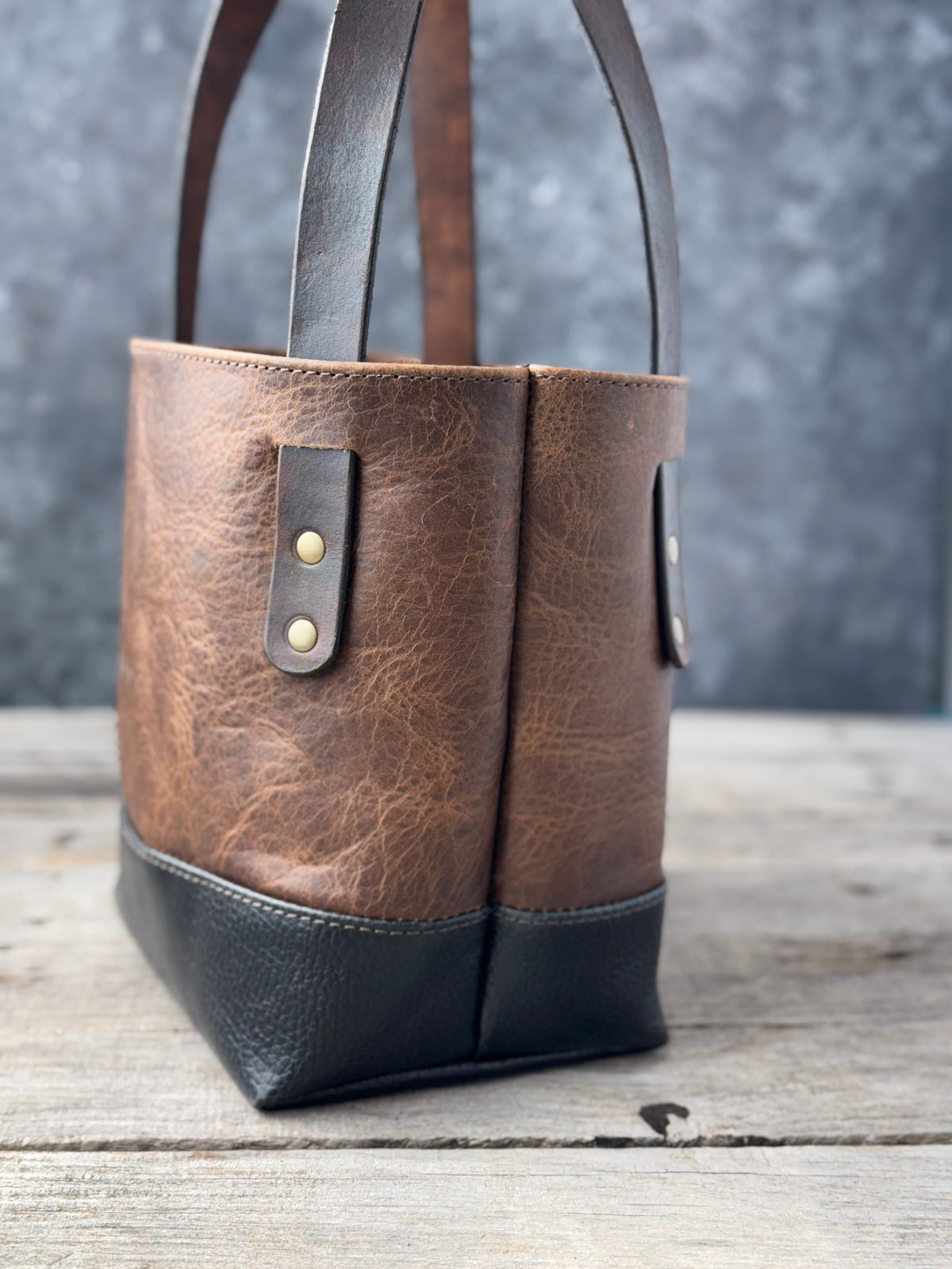 Side view of handmade bison leather tote with black pebbled base and antique brass strap rivets