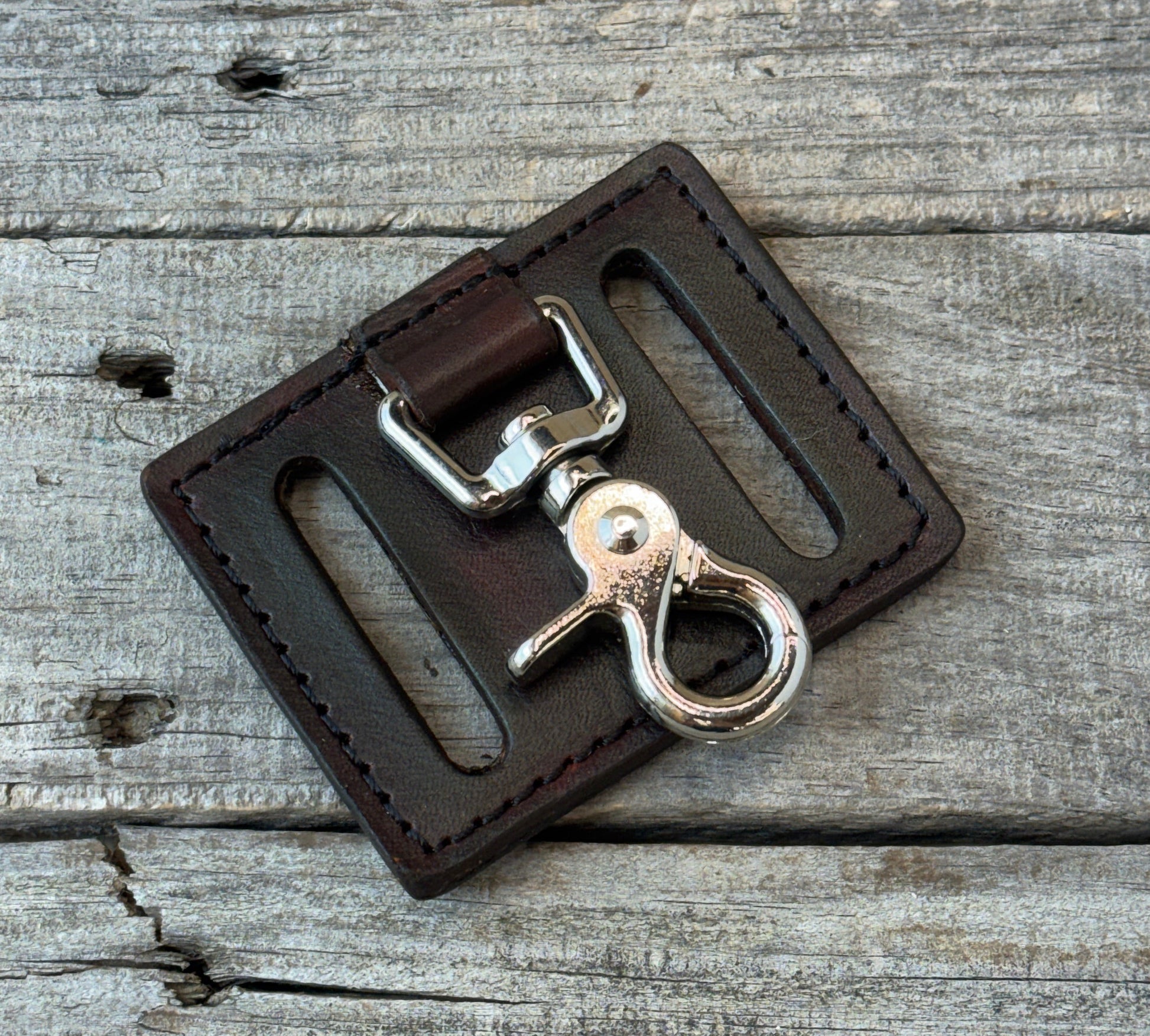Brown leather key fob with silver clasp on a wooden surface