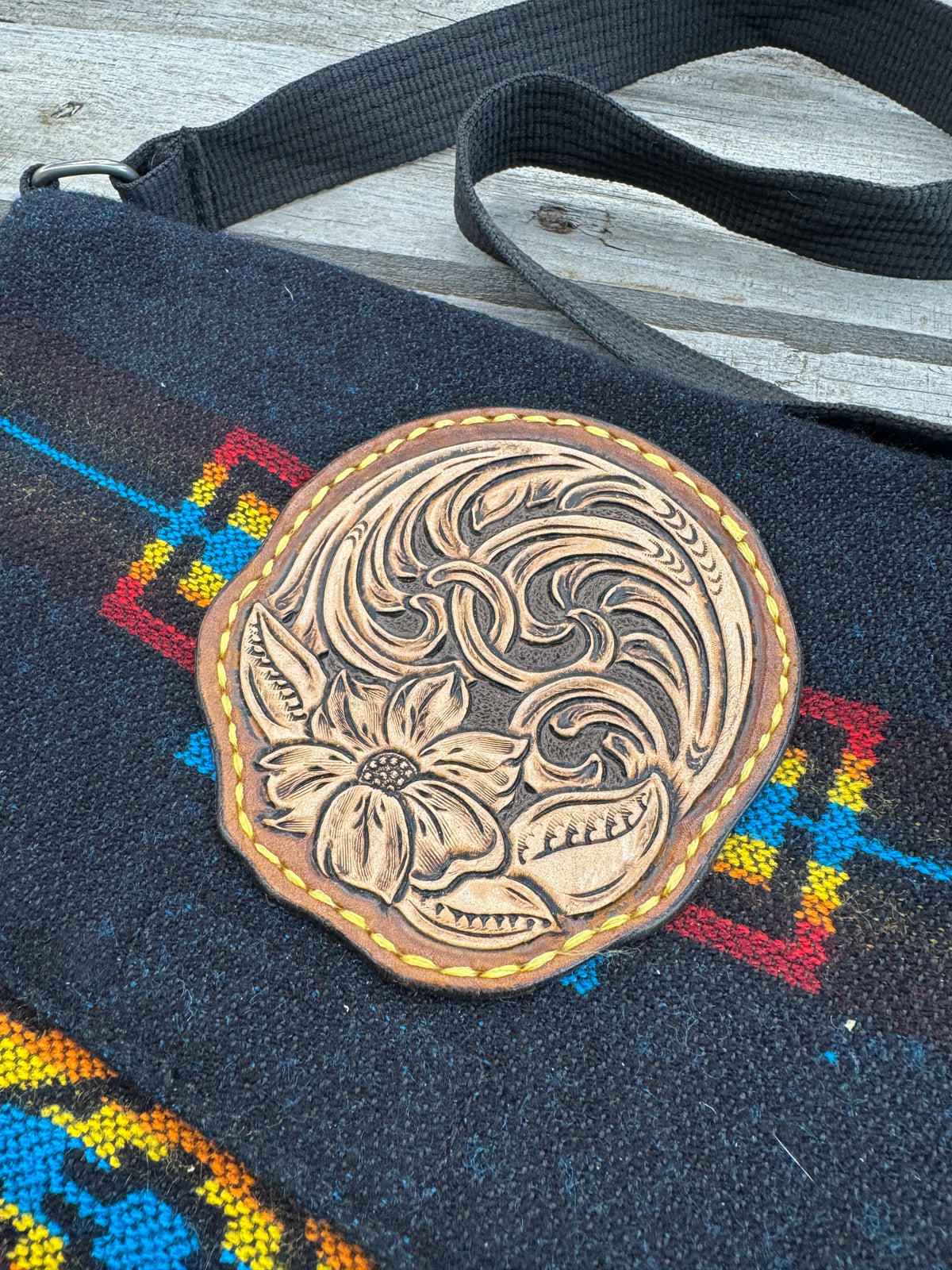 Black woven Southwest messenger bag with hand-tooled leather floral patch and yellow stitching, handmade by Cherokee Rose Custom Leather in East Texas.