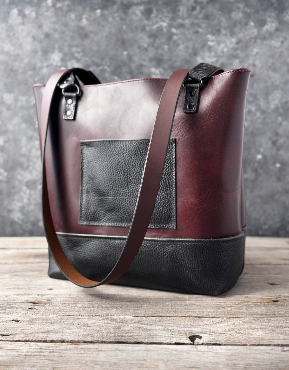 Handmade burgundy and black leather tote bag with exterior pocket, textured black base and brown shoulder straps