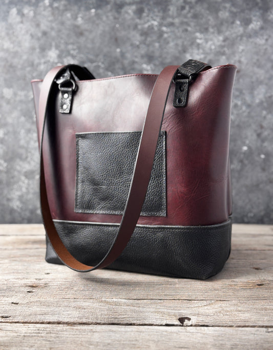 Handmade burgundy and black leather tote bag with exterior pocket, textured black base and brown shoulder straps