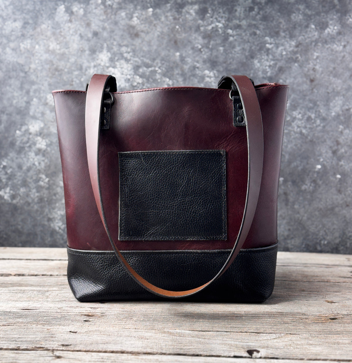 Back of burgundy leather tote bag with contrasting black leather bottom and riveted strap attachments