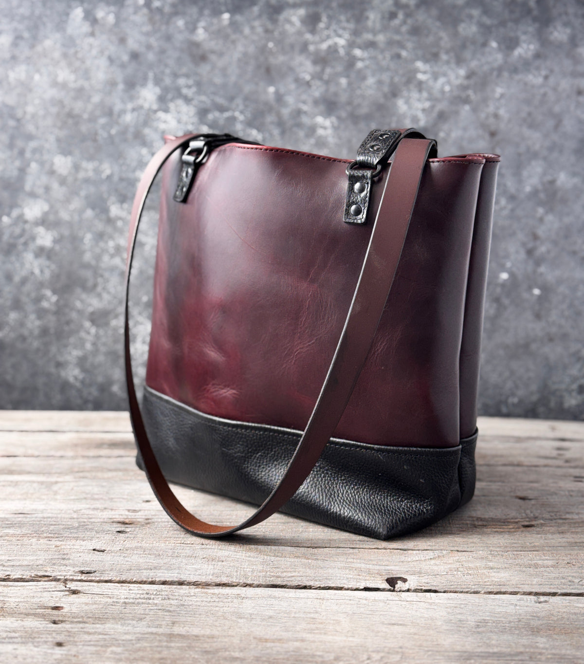 Close-up of burgundy and black leather tote with textured leather and black D-ring hardware