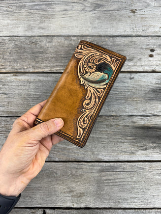 Hand holding a brown leather check book with intricate designs against a wooden background