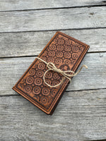 Brown embossed leather wallet tied with twine on a wooden surface