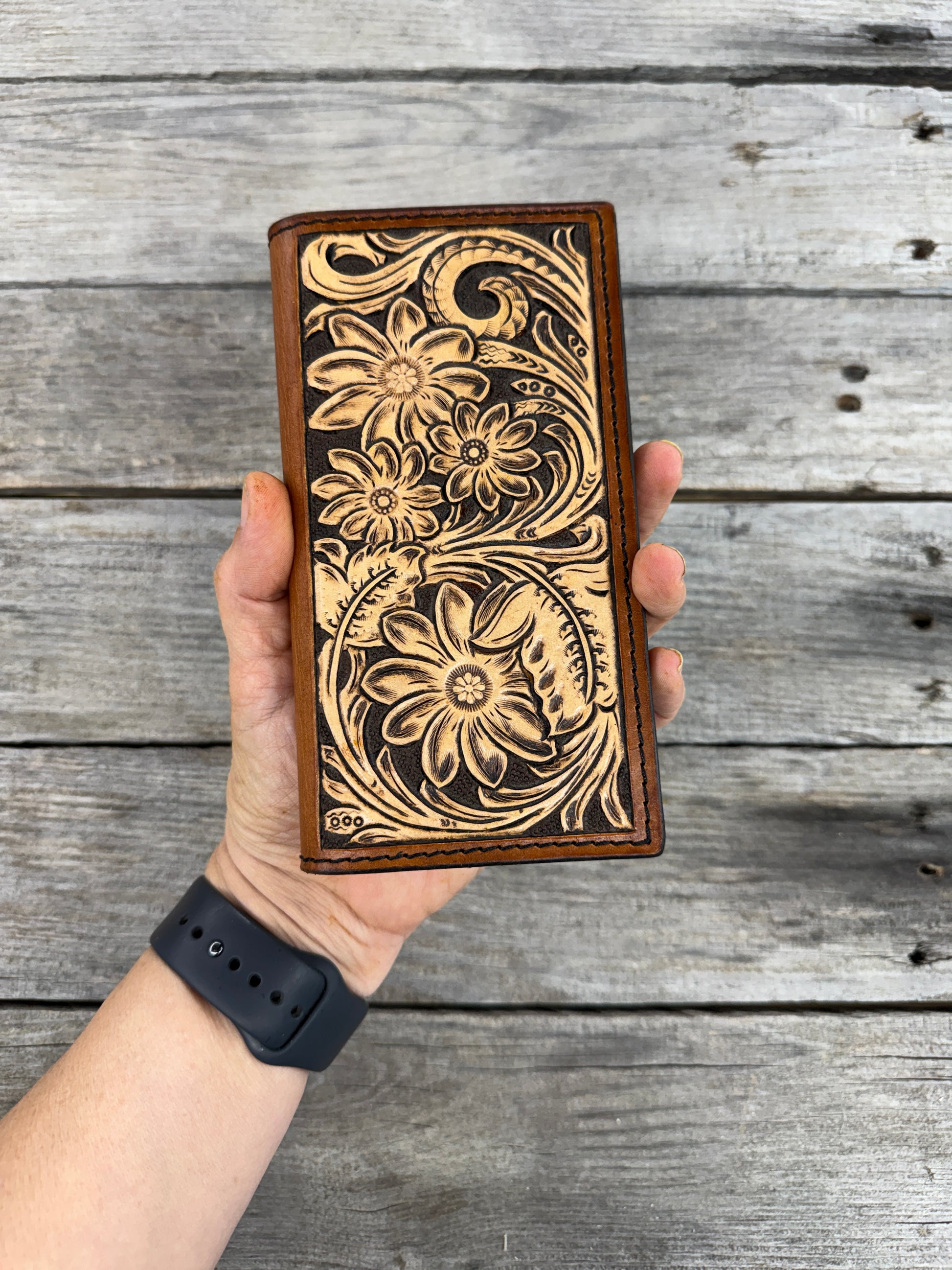 Handmade leather checkbook with floral patterns held against a wooden background