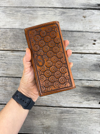 Hand holding a brown leather checkbook with embossed patterns against a wooden background