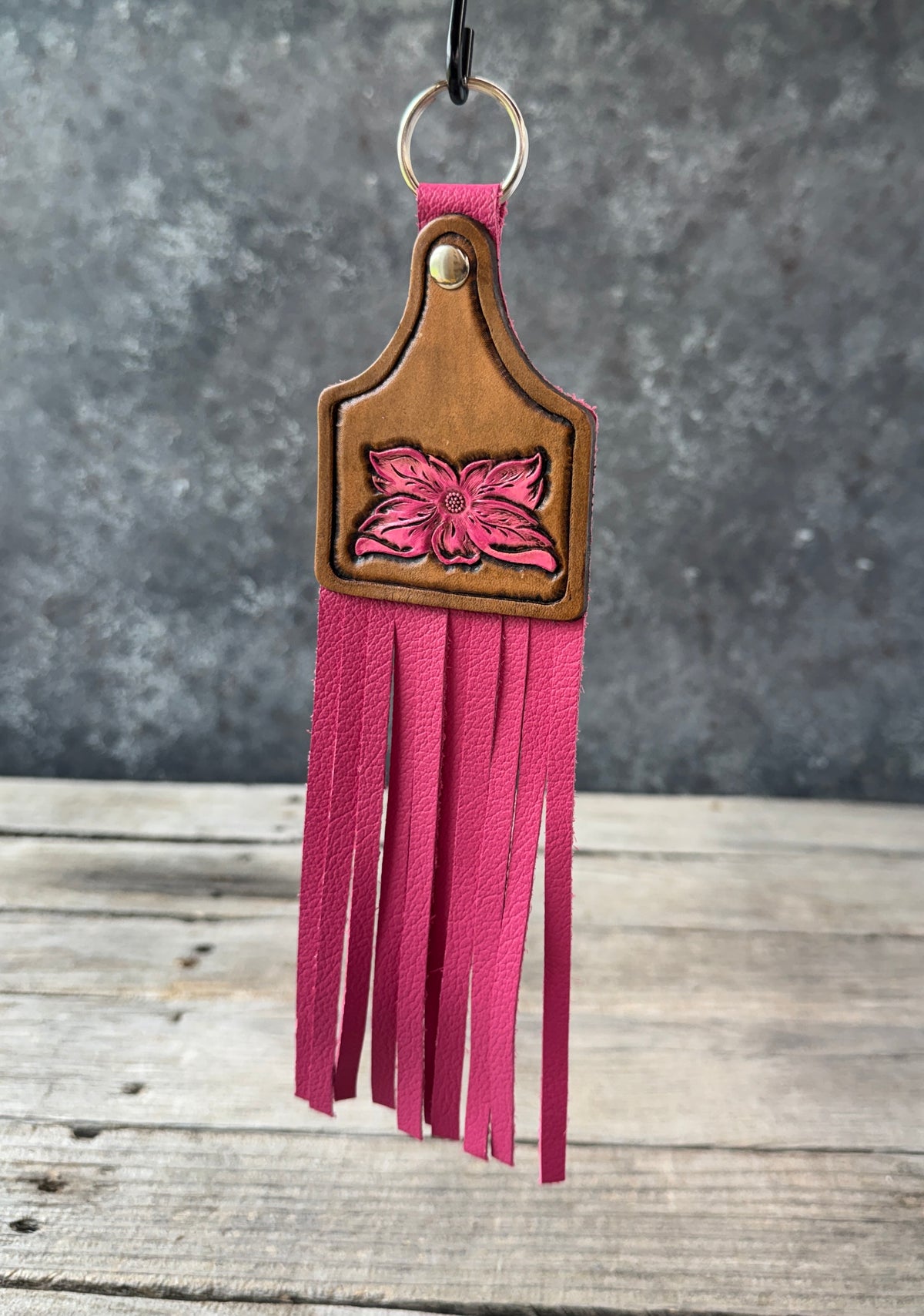 Leather keychain with pink fringe and floral design on a wooden surface