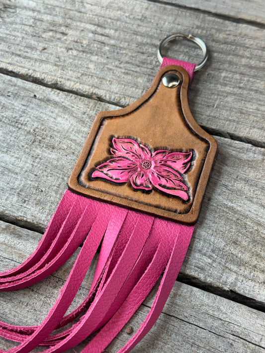 Leather keychain with pink flower design and fringes on a wooden surface