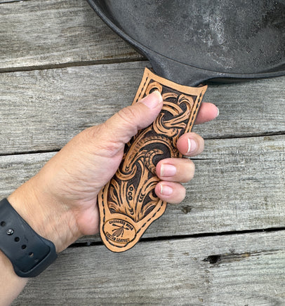 Hand tooled leather cast iron skillet handle cover with floral scroll carving and dyed background, handmade by Cherokee Rose Custom Leather in East Texas.
