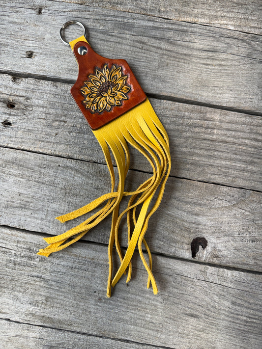 Carved Leather keychain with a yellow sunflower and fringe on a wooden surface