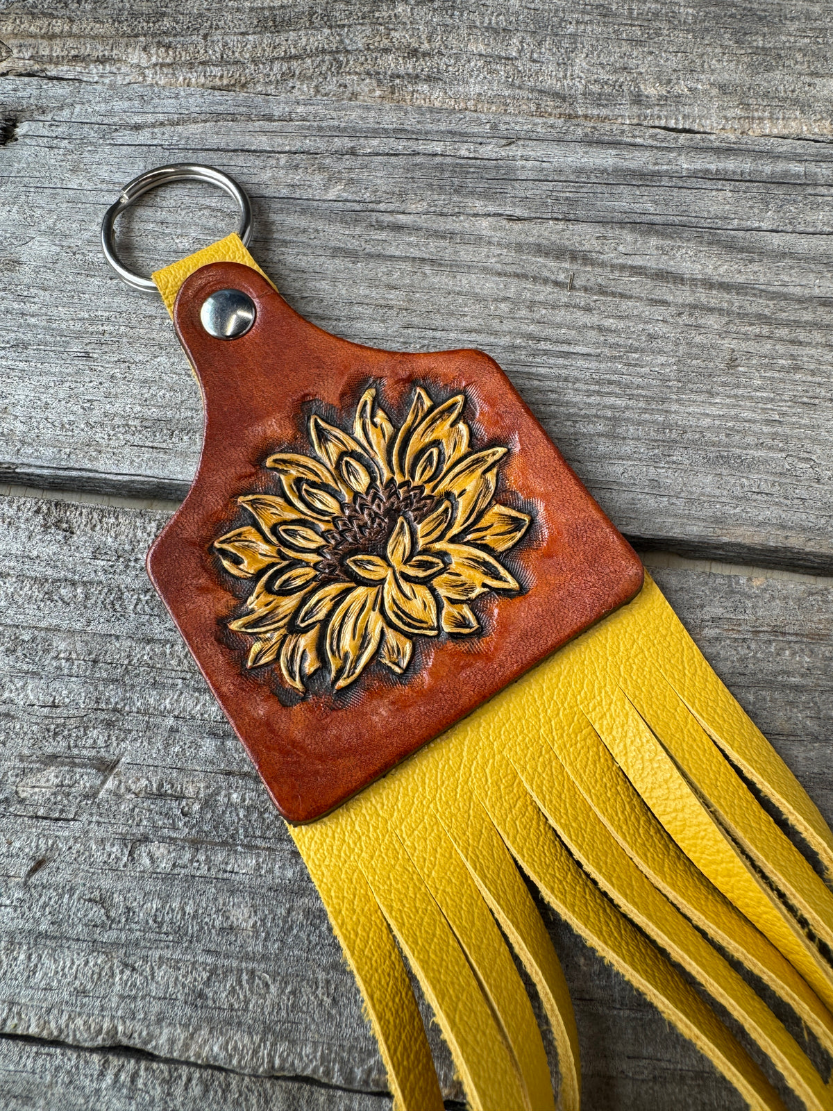 Leather keychain with sunflower design and yellow fringe on a wooden surface