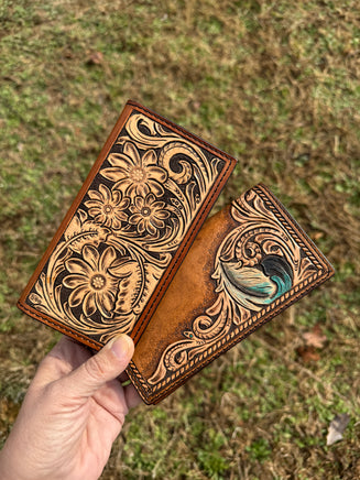 Two intricately designed leather wallets held by a hand against a grassy background