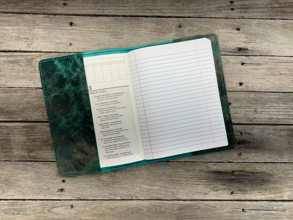 Open notebook with lined pages and a green leather cover on a wooden surface