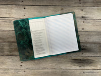 Open notebook with lined pages and a green leather cover on a wooden surface