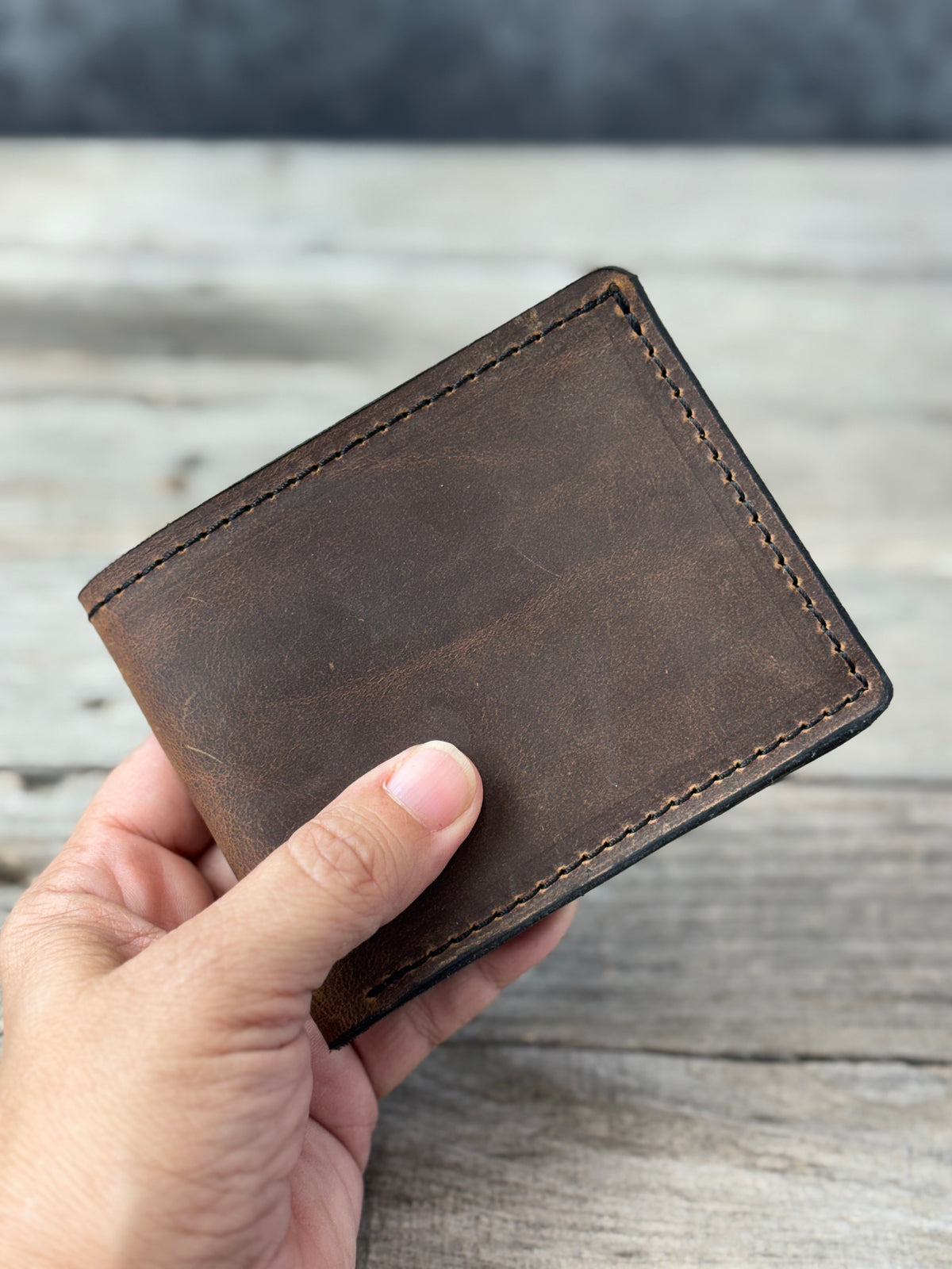 Dark brown oil tanned leather bifold wallet held in hand