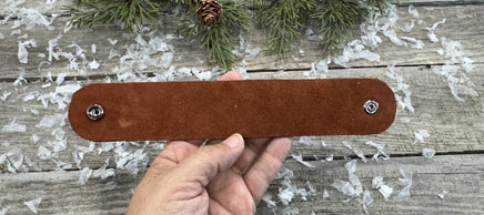 Hand-carved leather cuff bracelet with pink flower accent, gunmetal snaps, and brown suede lining, handmade by Cherokee Rose Custom Leather in Texas.