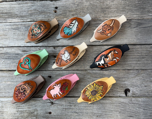 Collection of leather hair clips with various designs on a wooden surface