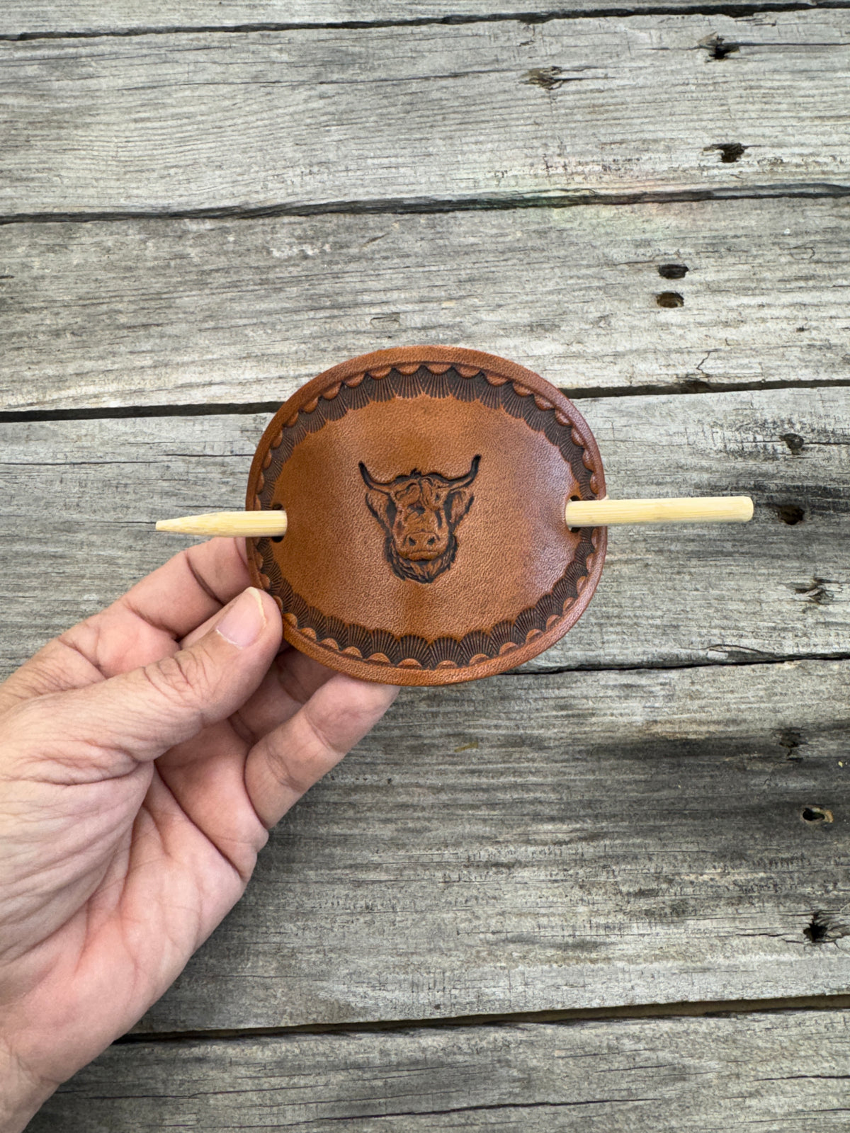 Hand holding a leather product with a hook against a wooden background