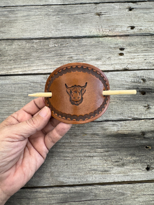 Hand holding a leather product with a hook against a wooden background