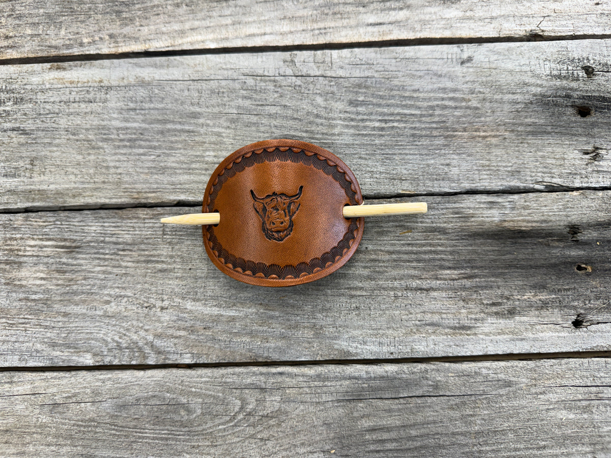 Round leather hair clip with engraved design on a wooden surface