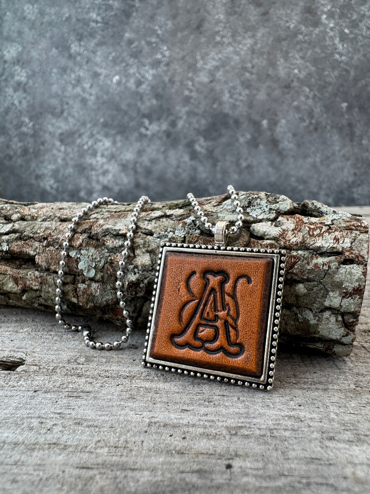 Floral Script letter A leather initial necklace styled on rustic wood with a silver ball chain