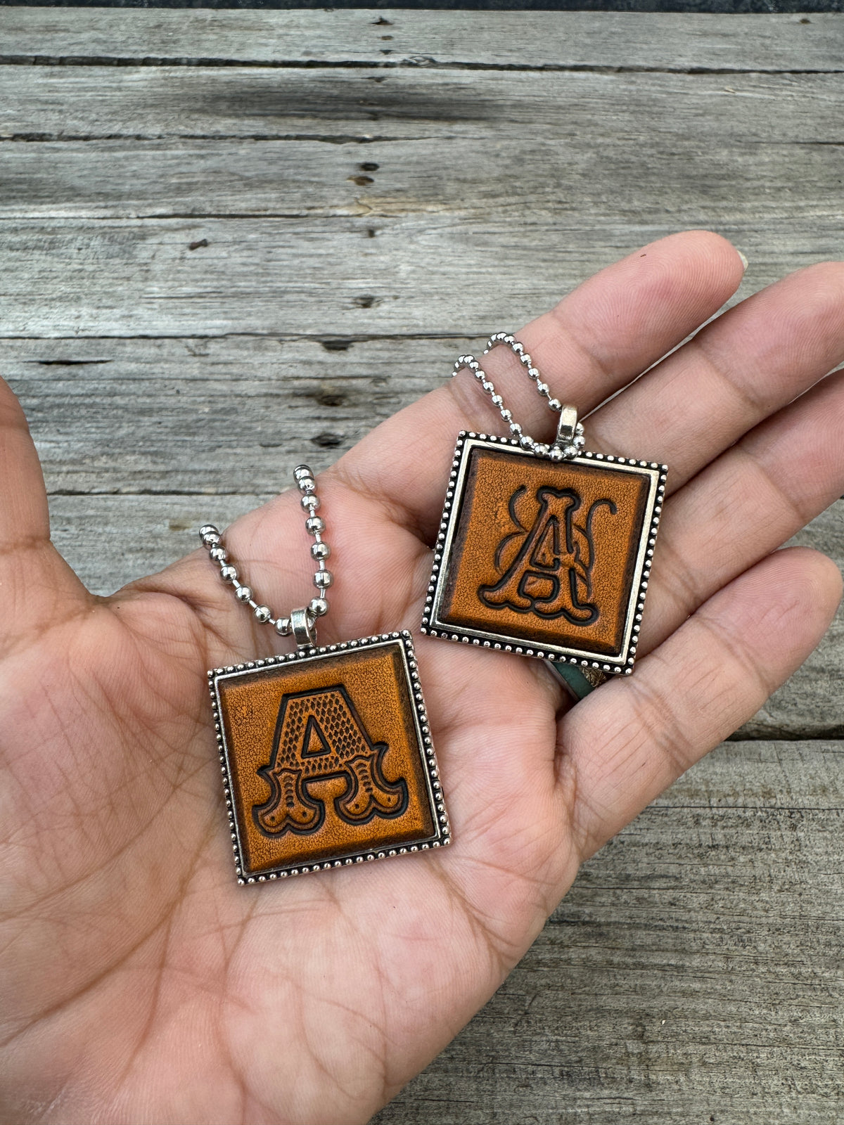 Western Block and Floral Script letter A leather pendants held in hand to show their 1-inch size