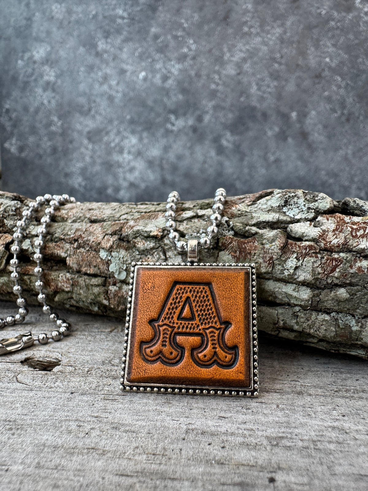 Western Block letter A leather initial necklace styled on rustic wood with a silver ball chain