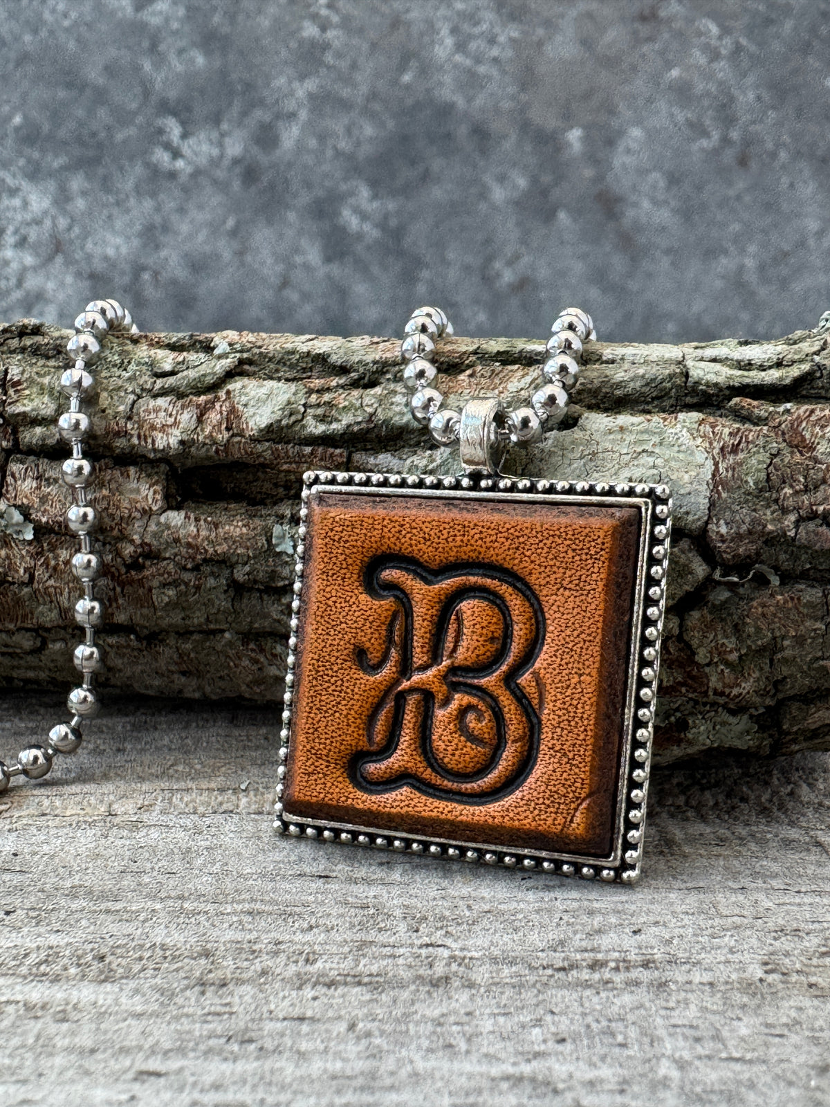 Floral Script letter B leather initial necklace styled on rustic wood with a silver ball chain