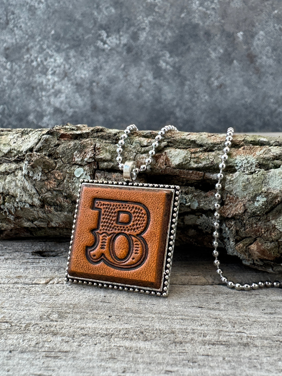 Western Block letter B leather initial necklace styled on rustic wood with a silver ball chain