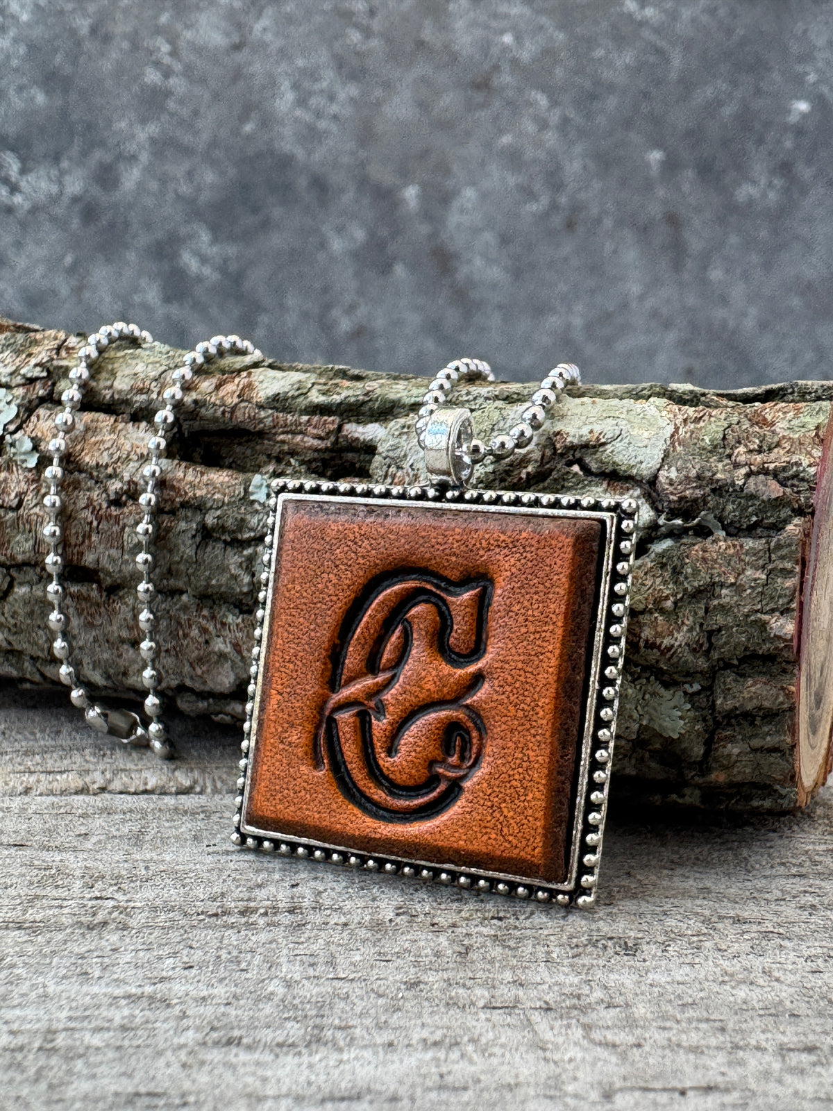 Floral Script letter C leather initial necklace styled on rustic wood with a silver ball chain