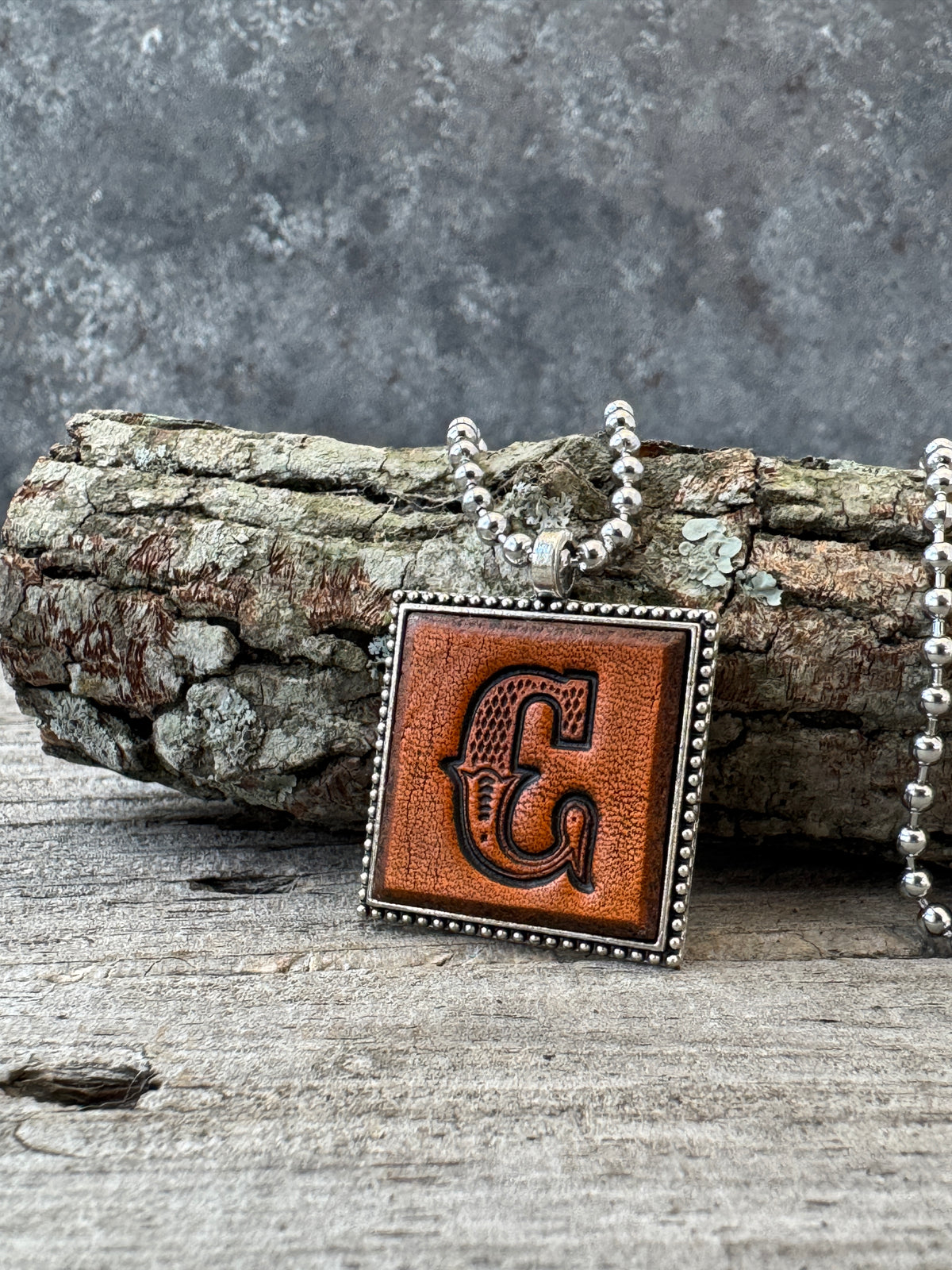 Western Block letter C leather initial necklace styled on rustic wood with a silver ball chain