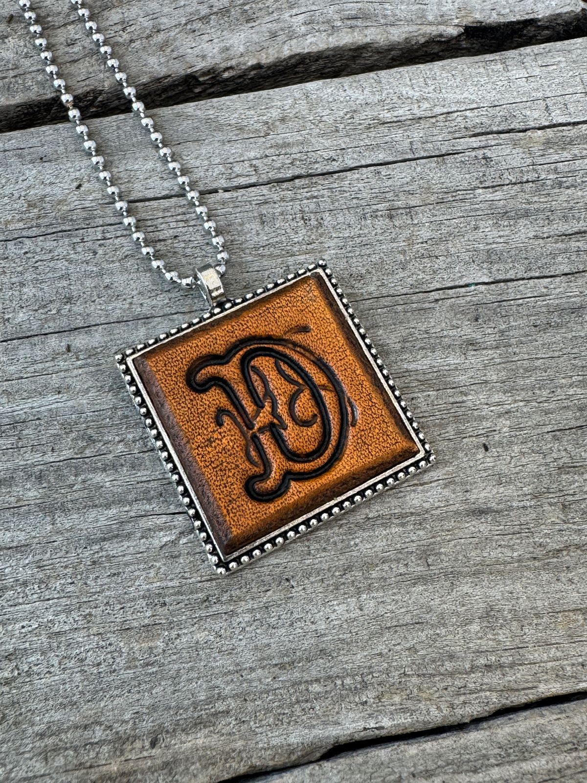 Floral Script letter D hand-stamped leather pendant necklace in a silver-tone square frame
