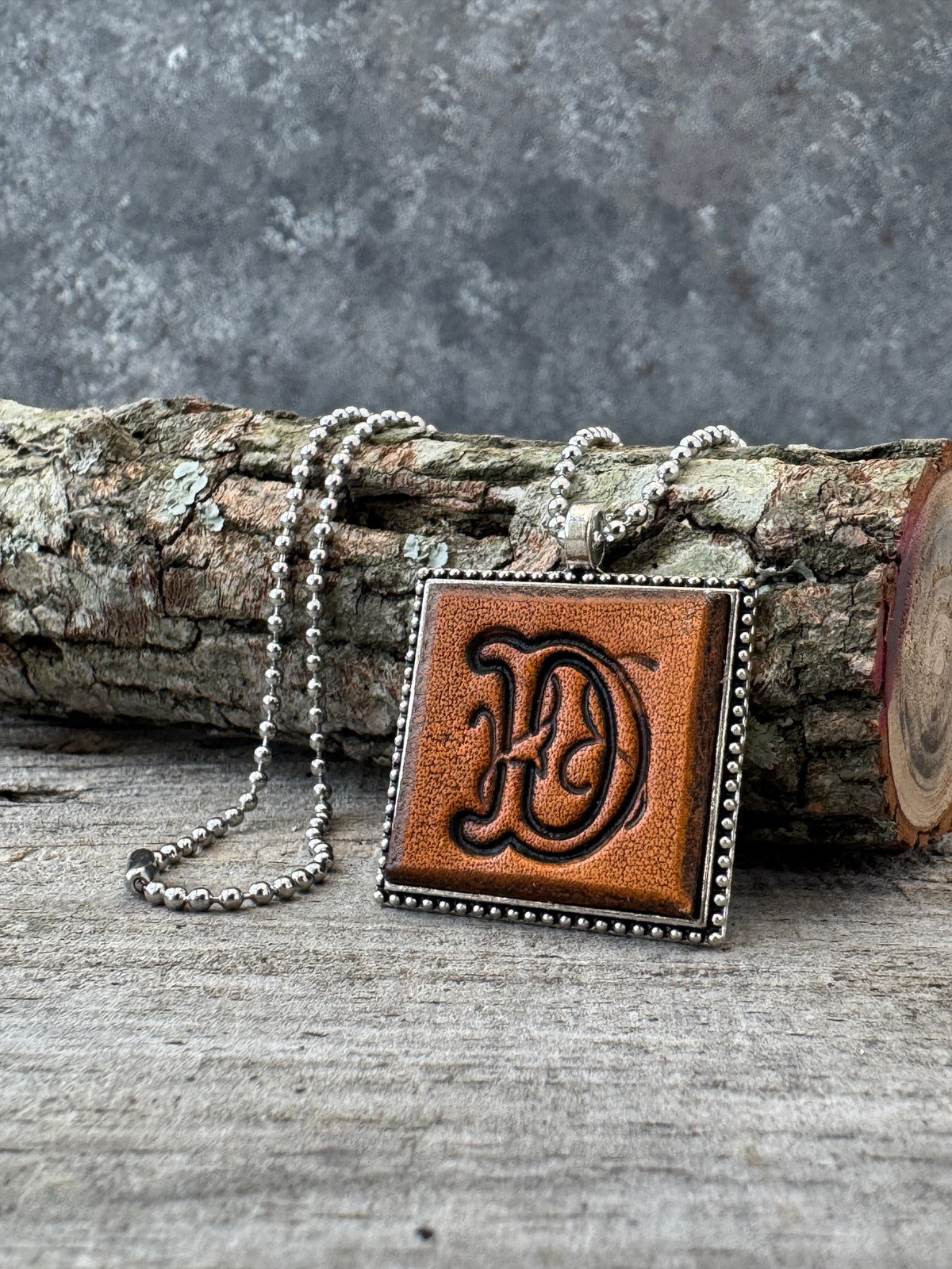 Floral Script letter D leather initial necklace styled on rustic wood with a silver ball chain
