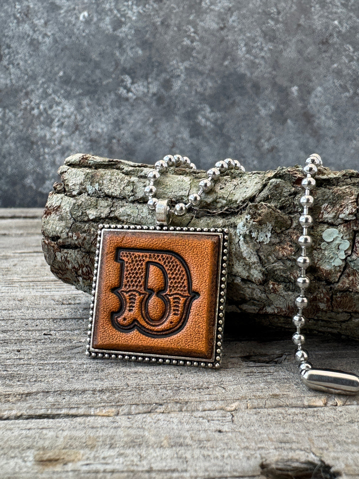 Western Block letter D leather initial necklace styled on rustic wood with a silver ball chain